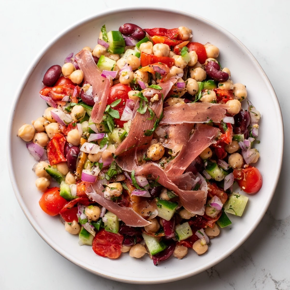 Vibrant dense bean salad with prosciutto, boasting fresh herbs, crisp veggies, and salty prosciutto ribbons.