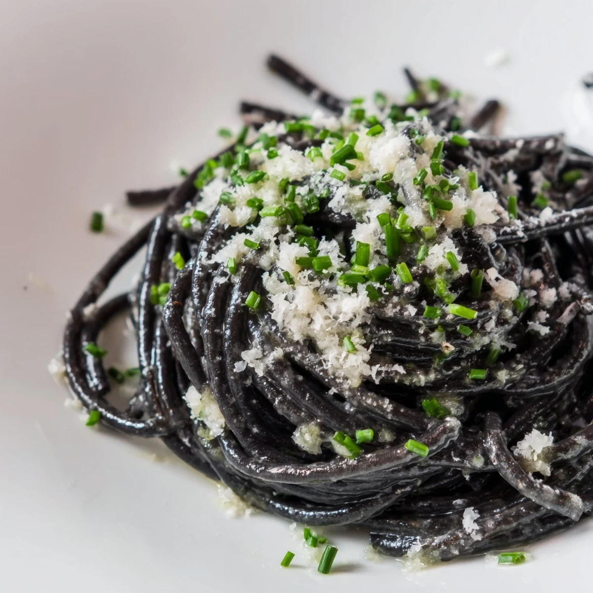 Plump black squid ink pasta glistens, coated in a creamy sauce, ready to serve with Parmesan.