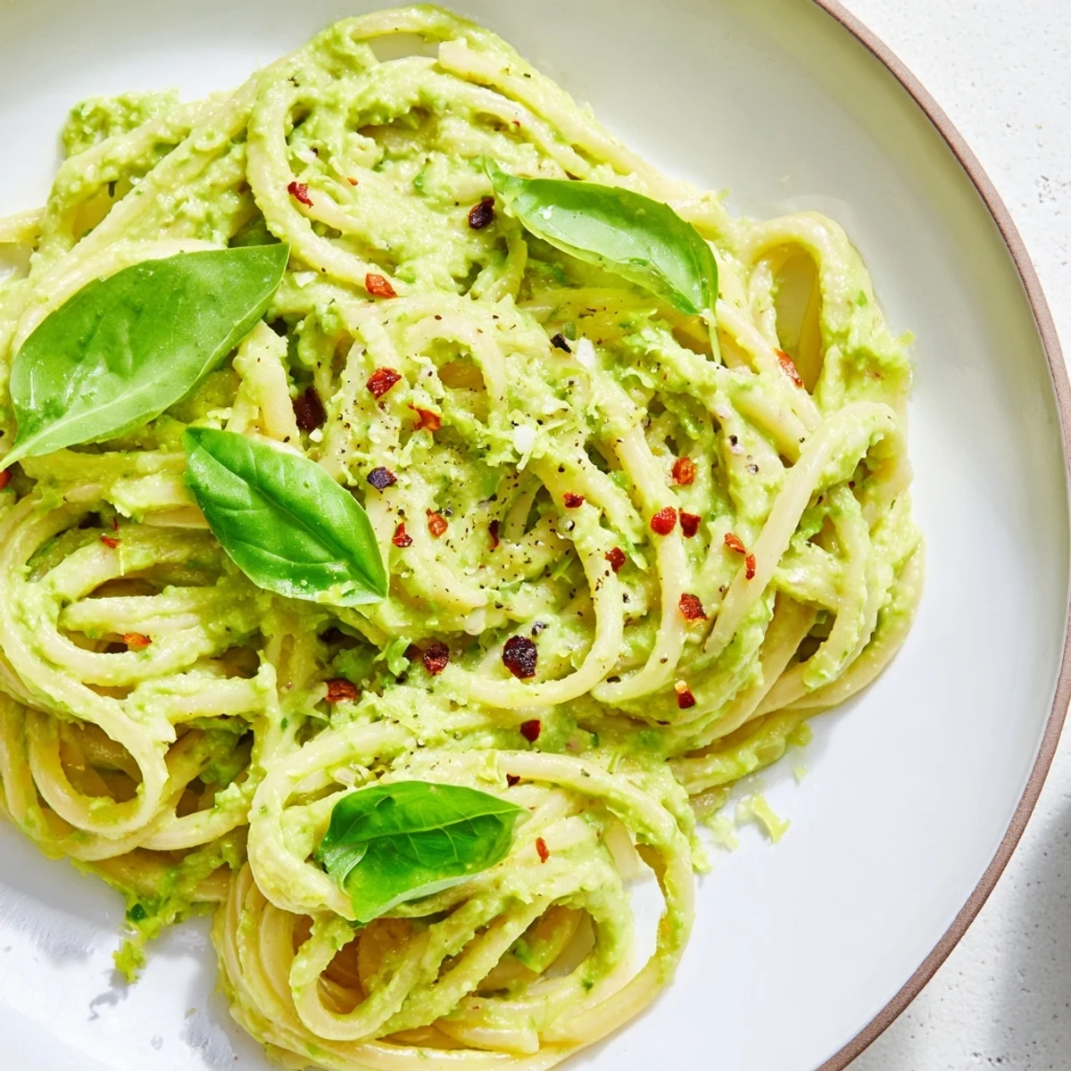 A close-up of creamy Smashed Avocado Pasta, garnished with fresh basil and red chili flakes.