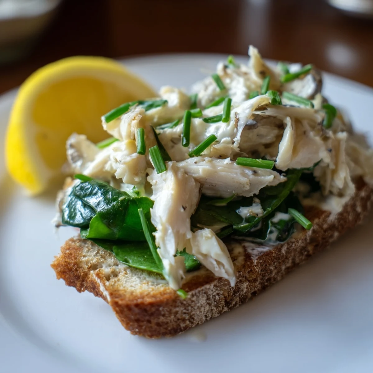 Close-up of smoked haddock rye toasts, featuring tender fish and fresh chives alongside a bright lemon wedge for serving.