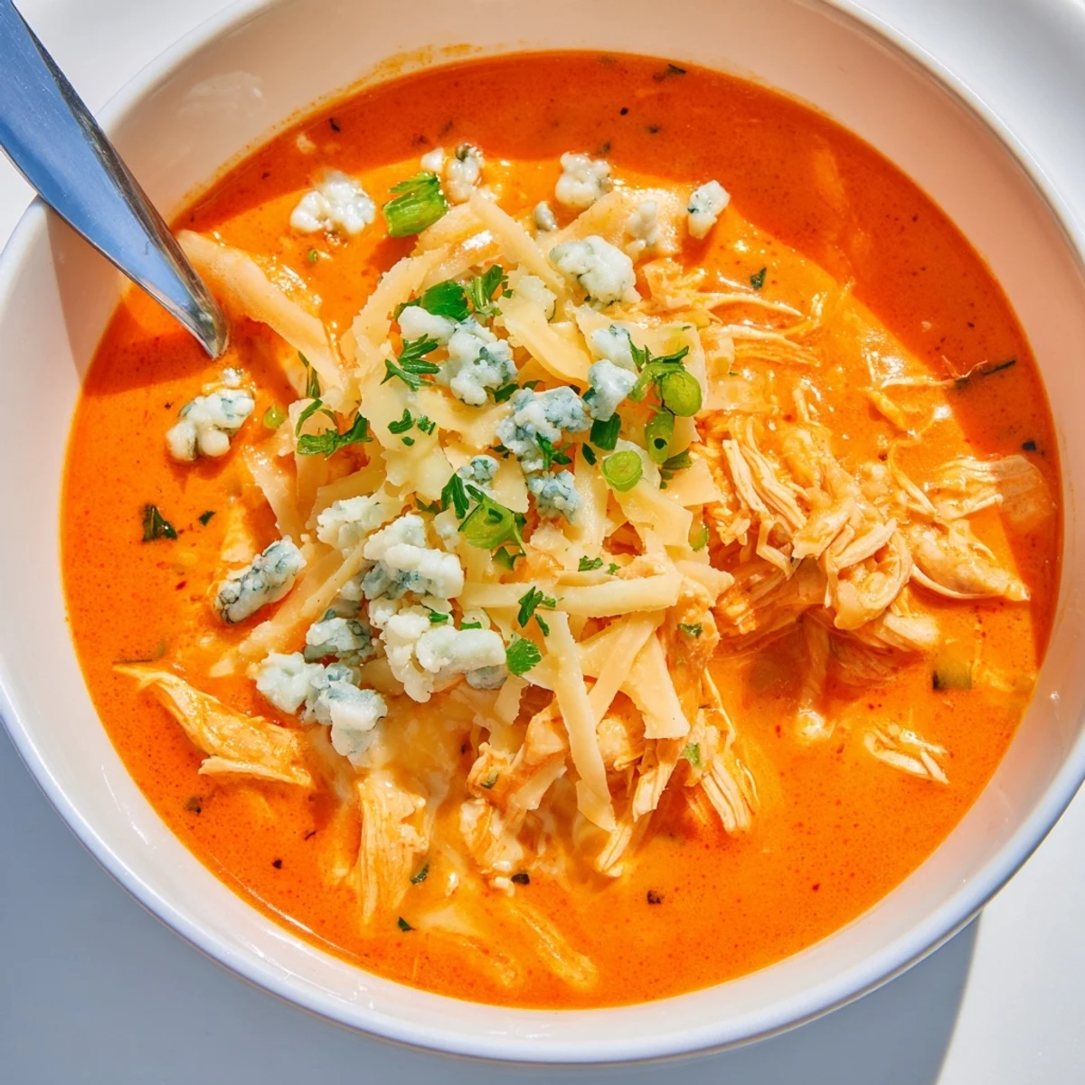 A close-up of velvety Crock Pot Buffalo Chicken Dip Soup, garnished with green onions and a sprinkle of blue cheese, served steaming in a rustic bowl.