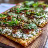 Freshly baked Goat Cheese & Caramelized Onion Flatbread with creamy cheese, sweet onions, and chili flakes on a wooden board.