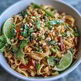 A close-up of Creamy Thai-Inspired Peanut Noodle Bowls with snap peas and red peppers coated in rich peanut sauce.