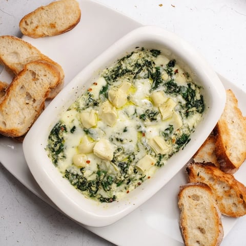 Creamy, bubbling Spinach Artichoke Dip served with golden toasted baguette slices for dipping.