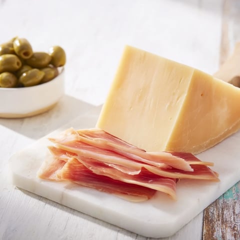 A minimalist cheese board featuring aged Comté, Jamón Ibérico, and Castelvetrano olives for elegant snacking.