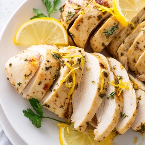 Golden Greek Lemon Herb Chicken breasts, perfectly seasoned, resting on a baking dish with vibrant herbs.
