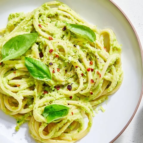 A close-up of creamy Smashed Avocado Pasta, garnished with fresh basil and red chili flakes.