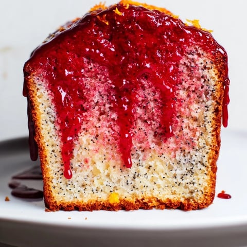Freshly baked blood orange loaf cake, studded with poppy seeds and marzipan, glistening with a ruby-red citrus glaze on a wooden board.  