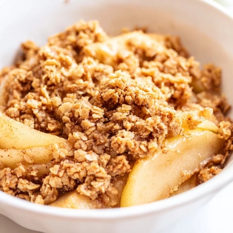Freshly baked pear crumble showcases bubbling golden pears beneath a thick, crunchy oat topping, ready to enjoy.