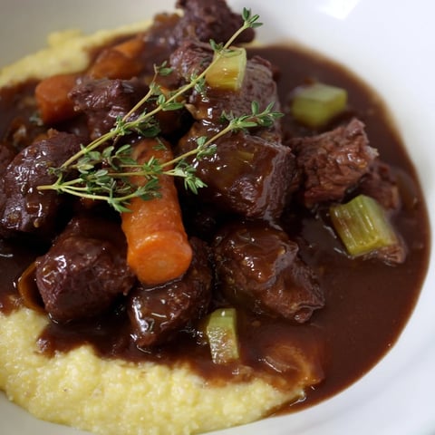 A close-up of rich Venison Stew with Sloe Gin and Polenta, with tender meat pieces nestled in a glossy, dark sauce.
