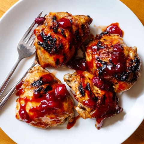 Grilled chicken thighs coated in sweet cherry bourbon BBQ sauce, garnished with fresh herbs.  