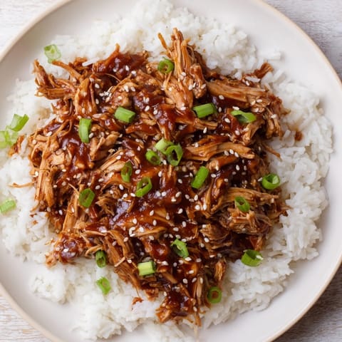 A steaming bowl of Easy Slow Cooker Teriyaki Chicken with rice, garnished with green onions and sesame seeds.