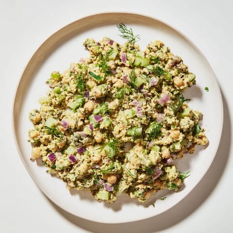 A close-up of a bowl of chickpea tuna salad, with visible chunks of vegetables mixed in.
