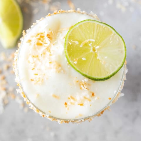 A vibrant White Christmas Margarita Slush, blended to a perfectly frosty cocktail with lime wedges.