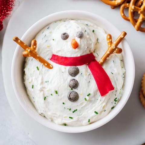 A close-up of the Melted Snowman Dip showcases creamy dip with pretzel arms, red pepper scarf.