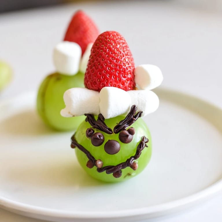Festive Grinch Snack featuring green grapes, fluffy marshmallows, and strawberry hats are perfect for holiday fun.