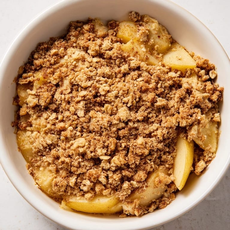 A scoop of vanilla ice cream melts over a golden baked pear crumble, creating the perfect comforting dessert.