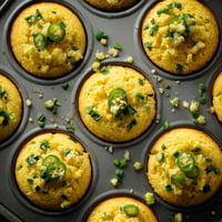 A tray of yellow muffins with green toppings.