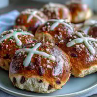 Freshly baked hot cross buns with citrus glaze, golden and soft, dotted with dried fruit and topped with a glossy orange-lemon drizzle.